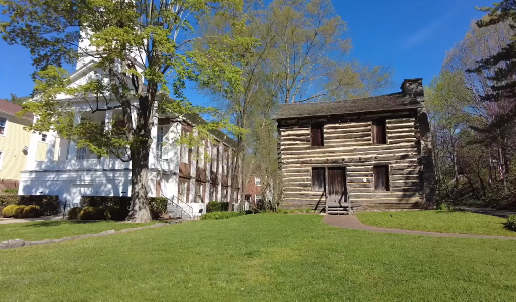 white house and wooden old buildings on the grass, trees between them